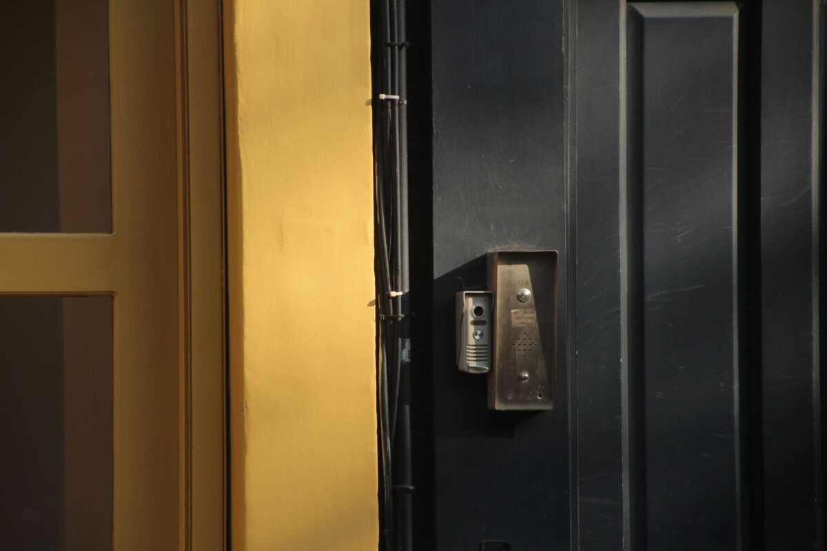 A close-up view of a dark door with a yellow frame and a metallic intercom system.